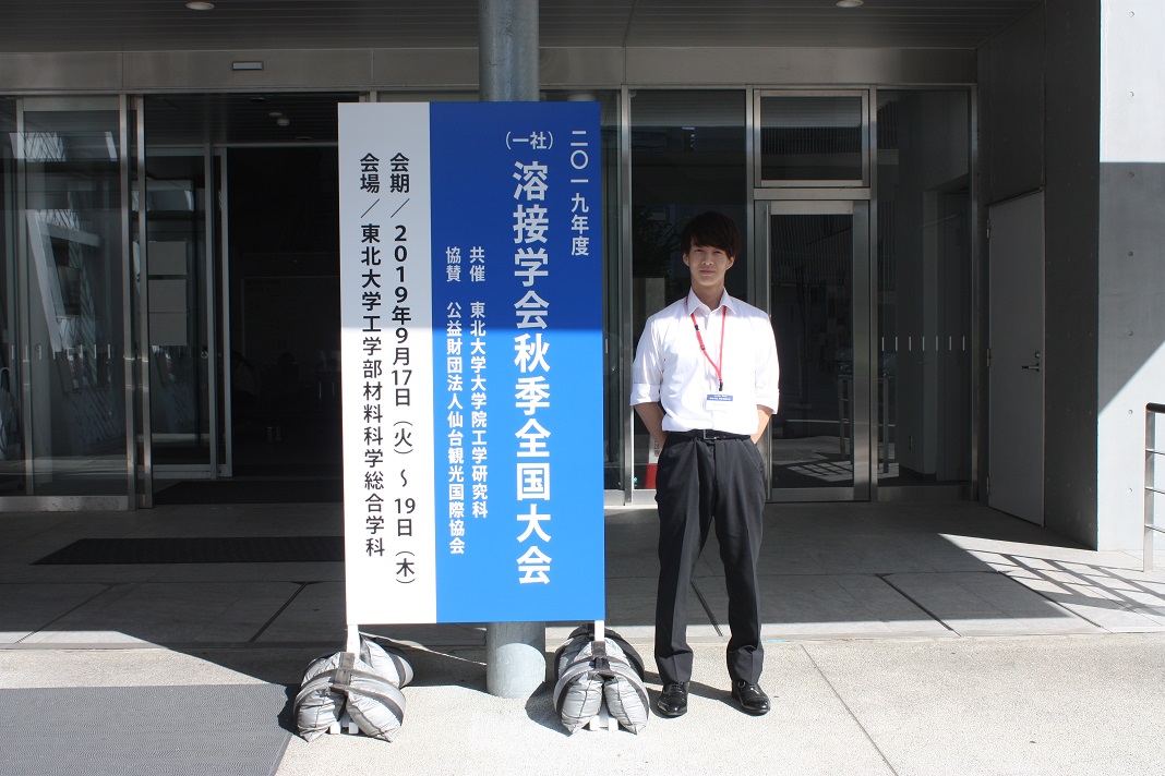 看板の横で記念撮影するけんや