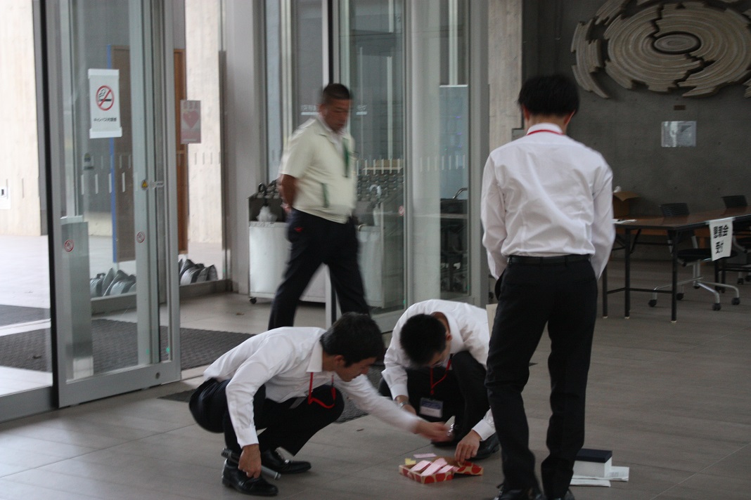 小さな紙が入った箱をひっくり返してしまった酒井とそれを助ける下川さんと打越